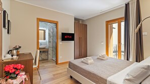 Una habitación de hotel con cama, escritorio con silla, televisión, baño y balcón.