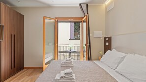 Habitación de hotel con cama, armario de madera, balcón con mesa y sillas, y planta en maceta.