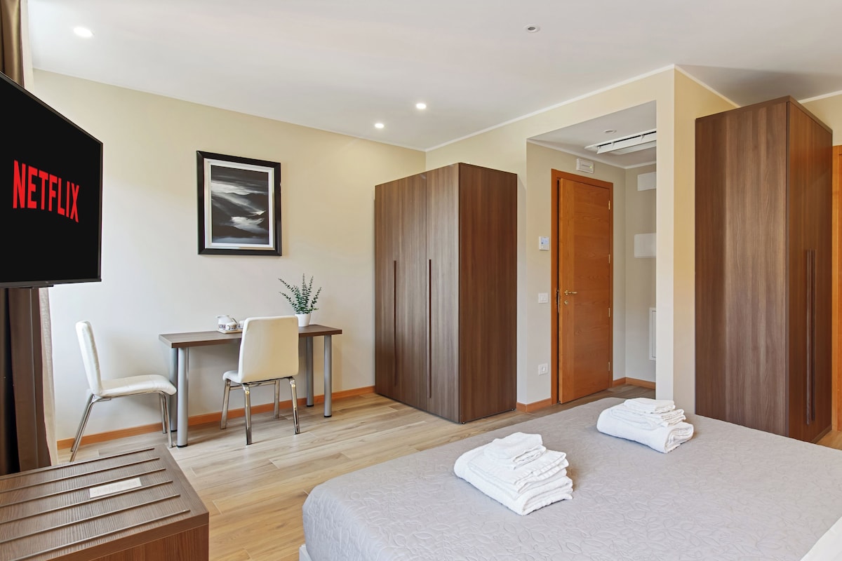 A hotel room with a bed, a desk, a chair, a TV, and a bathroom.