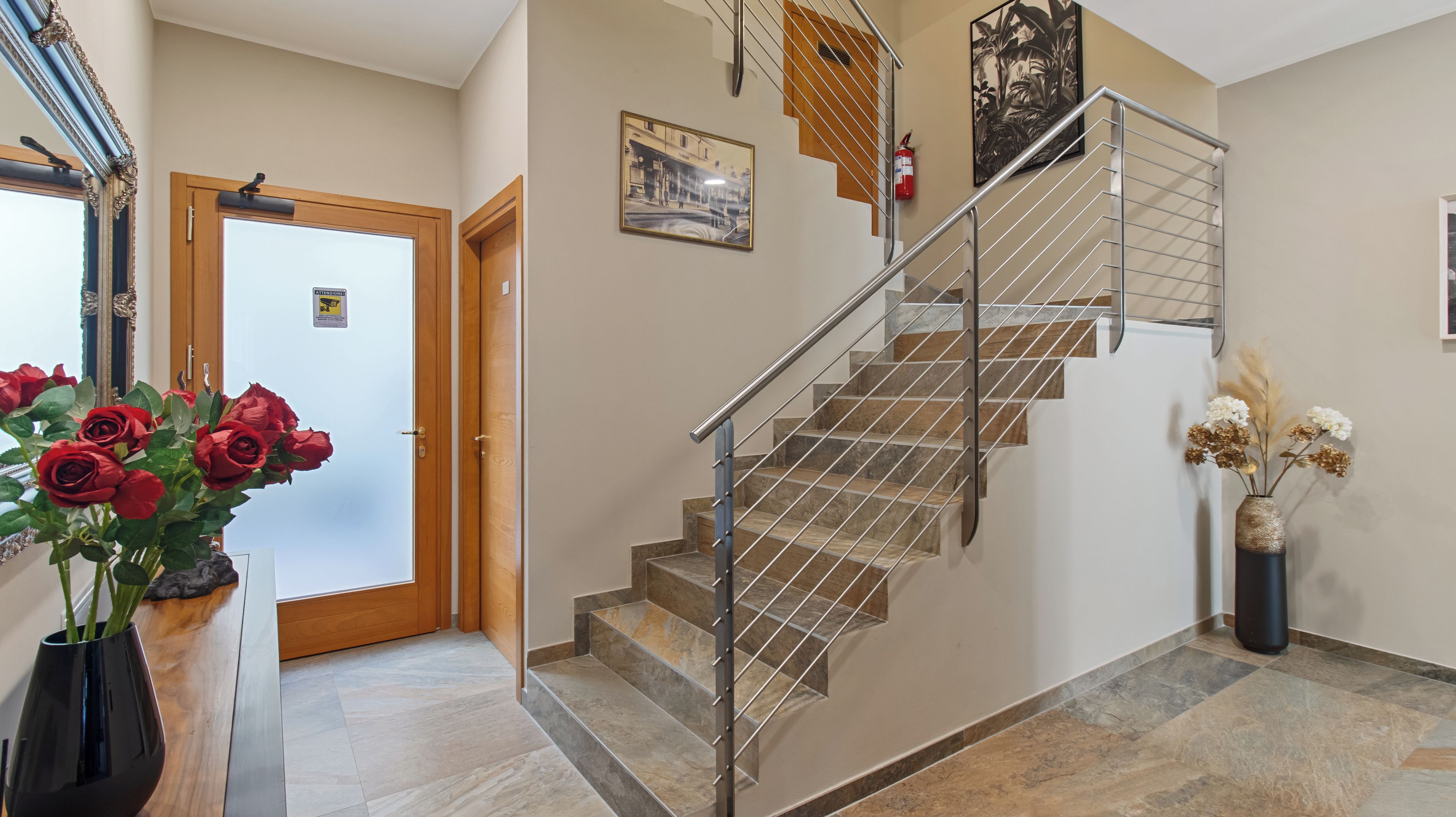 Un escalier avec une rampe en métal, une porte en bois et un vase rempli de fleurs.