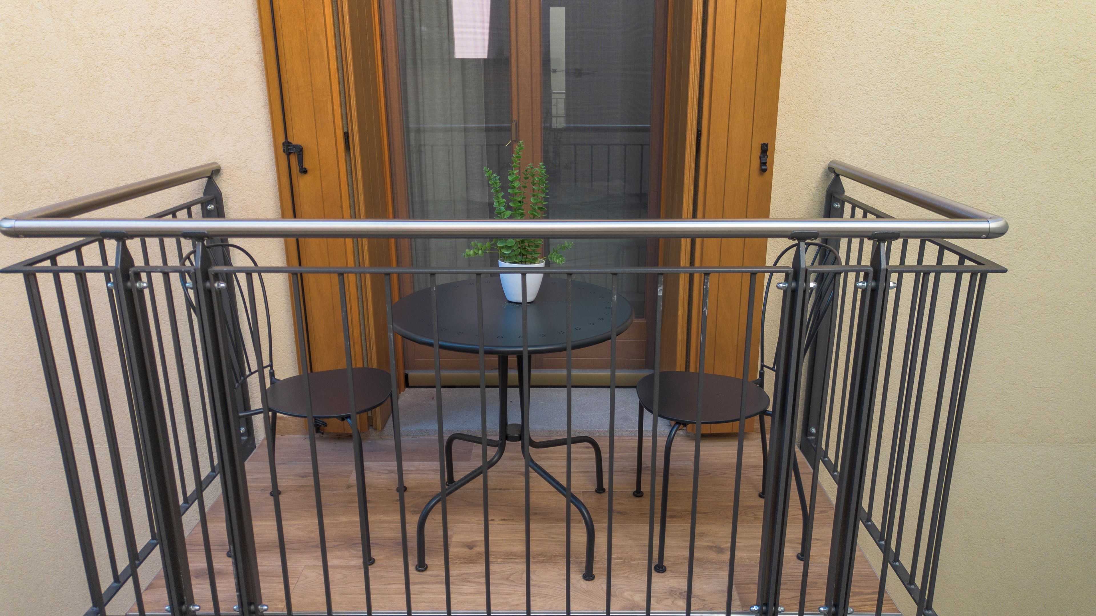 Un balcón con baranda metálica, una pequeña mesa redonda, dos sillas y una planta en maceta.