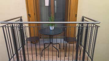 Un balcón con baranda metálica, una pequeña mesa redonda, dos sillas y una planta en maceta.