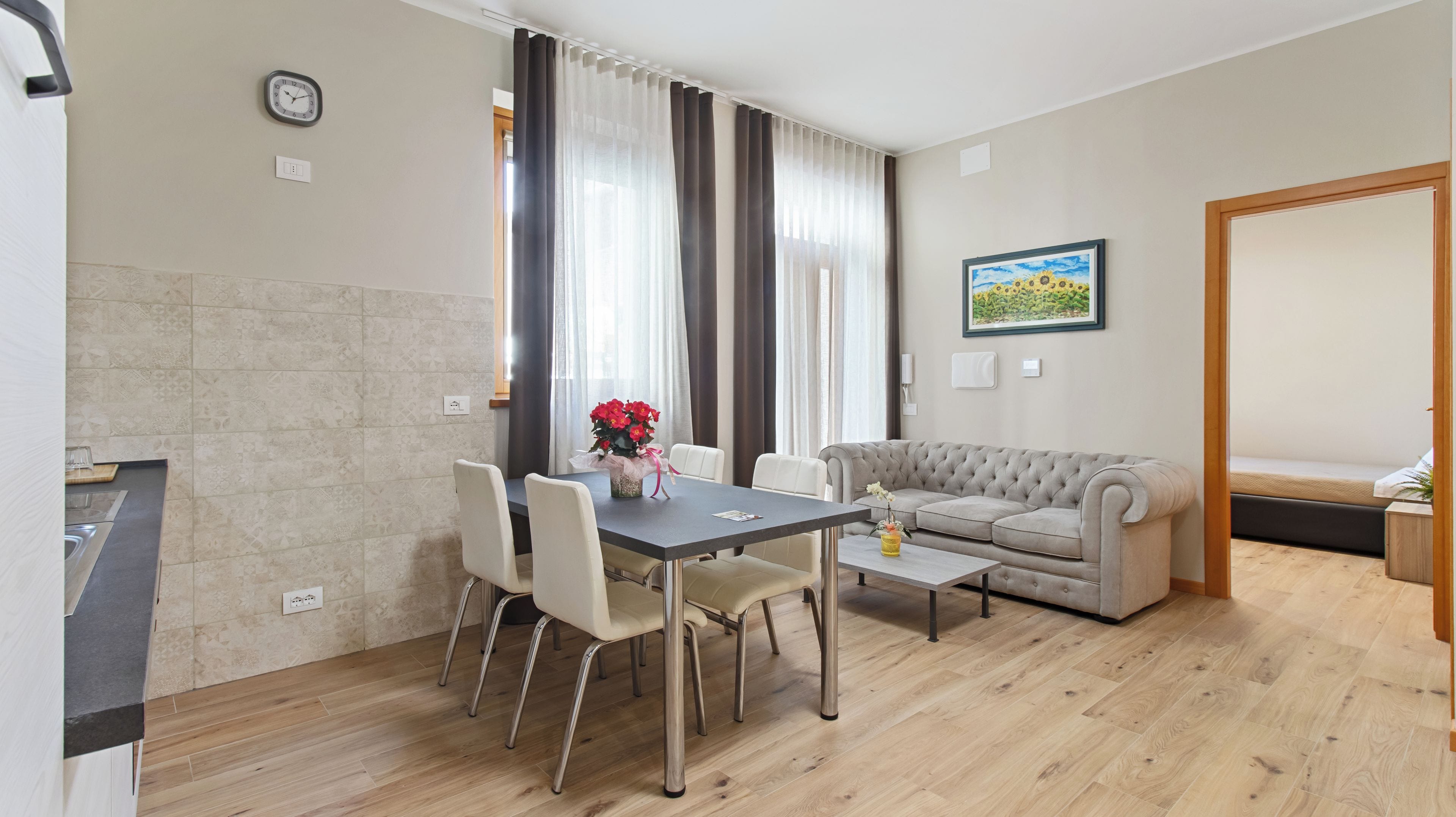 Ein Essbereich mit Tisch, Stühlen und einer Couch. An der Wand hängt eine Uhr, über der Couch ein Gemälde.