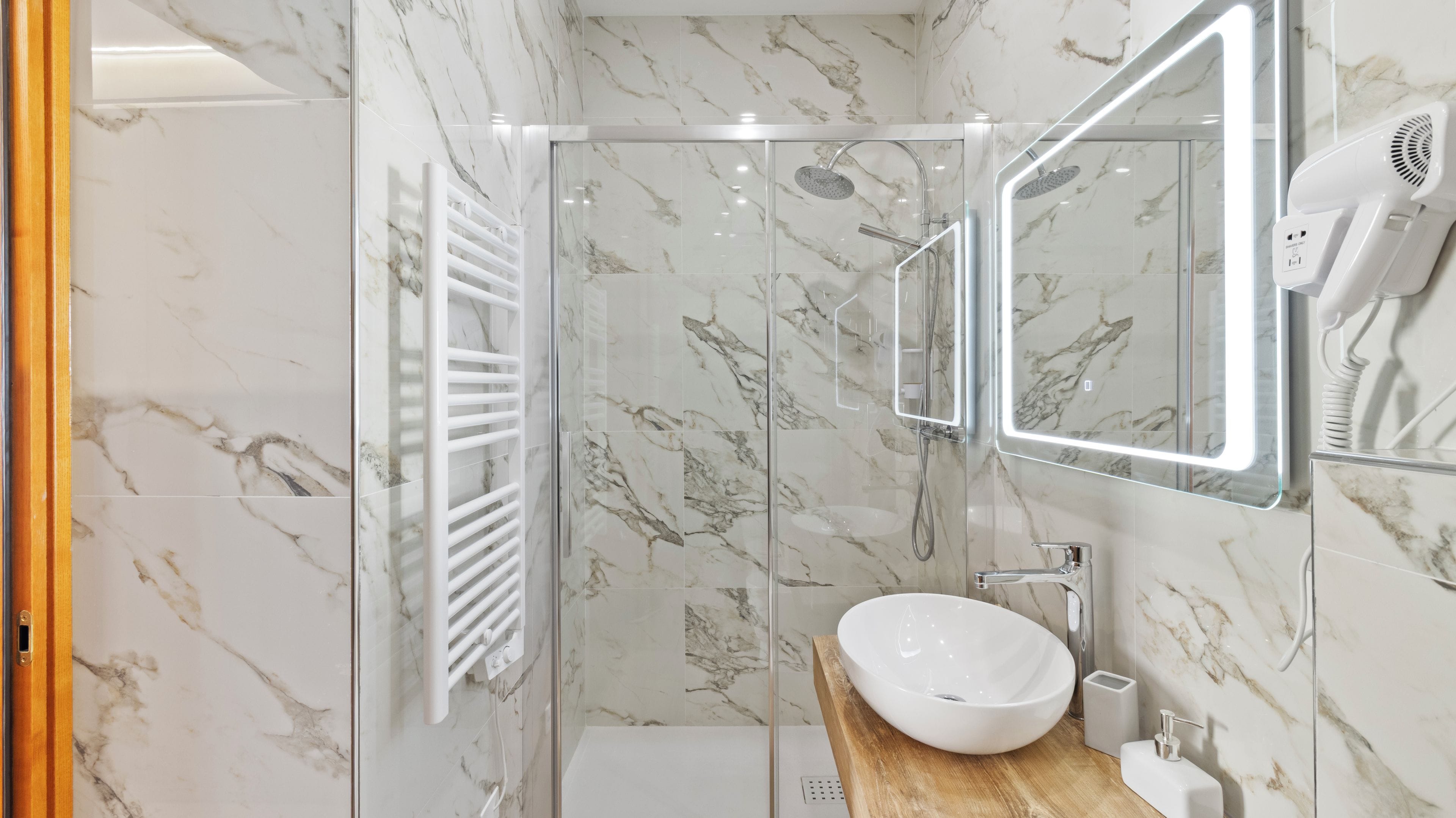 Un bagno moderno con doccia vetrata, lavandino bianco e asciugacapelli montato a parete.