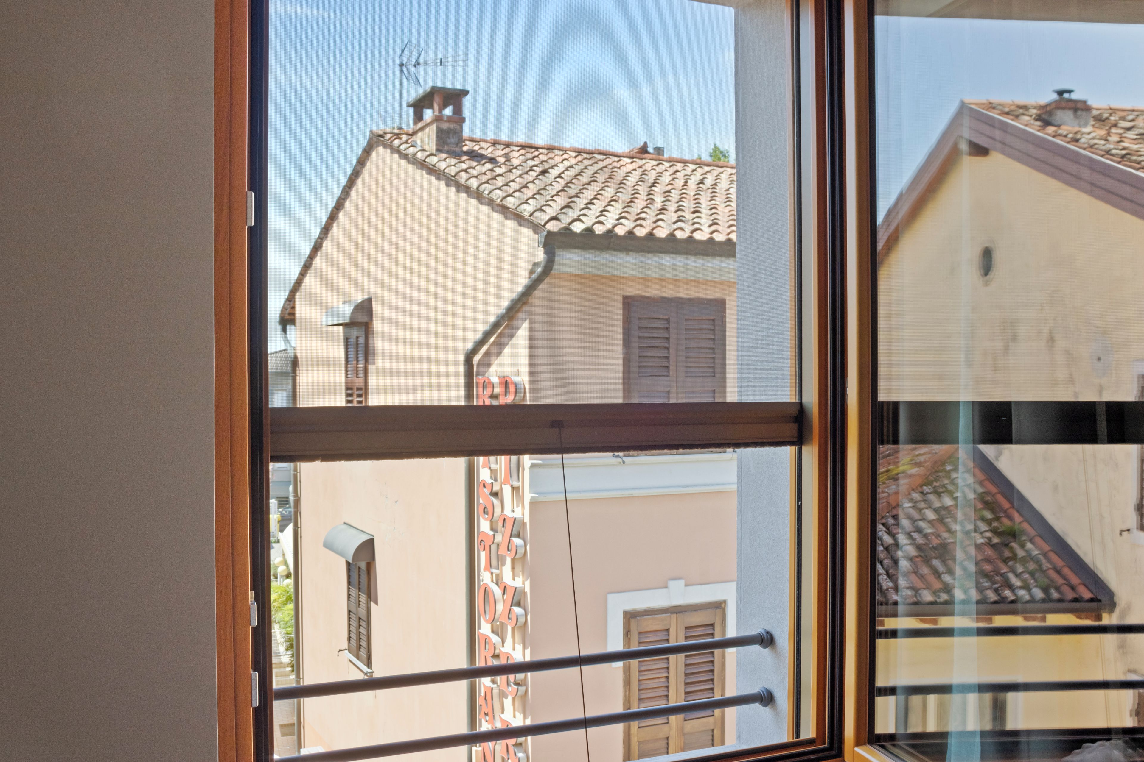 Une fenêtre donnant sur la façade d’un bâtiment, avec vue sur un toit recouvert de tuiles et une cheminée.