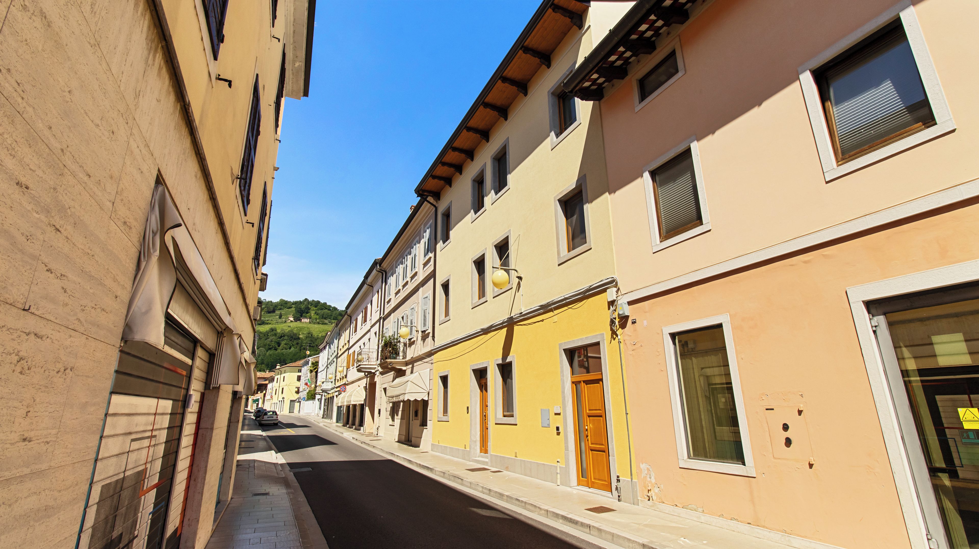 Una calle estrecha flanqueada por edificios de varios pisos, algunos con balcones y ventanas, bajo un cielo despejado.