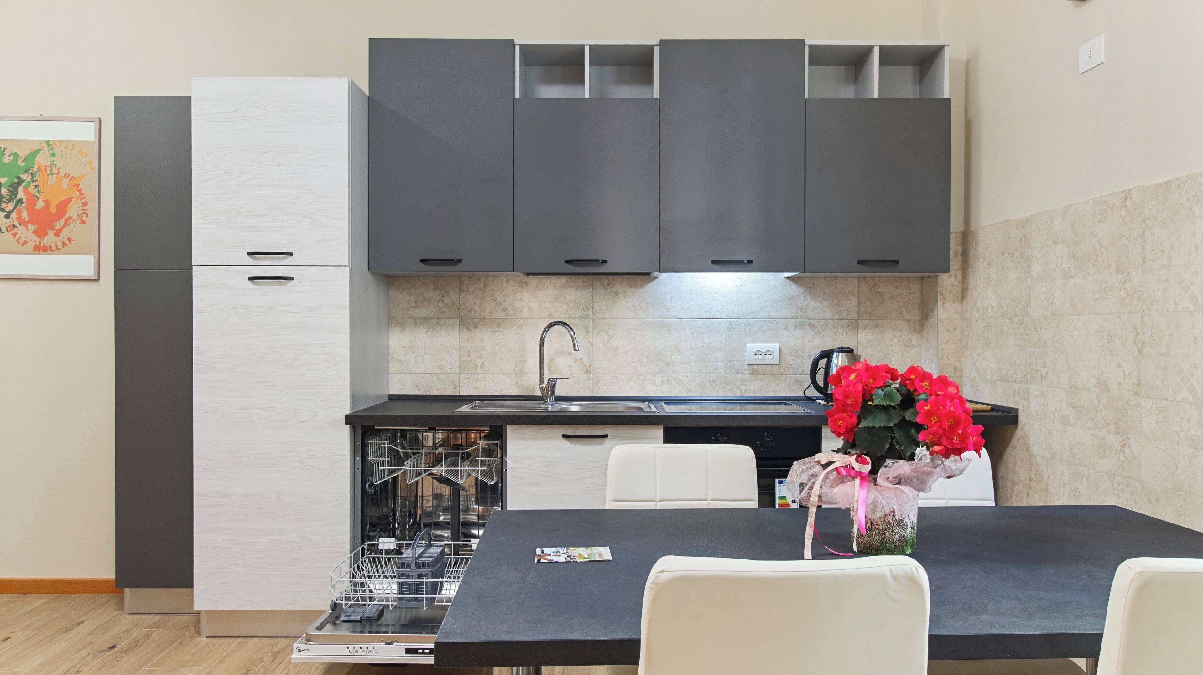 Una cocina moderna con armarios grises, encimera negra y una mesa de comedor blanca con sillas.