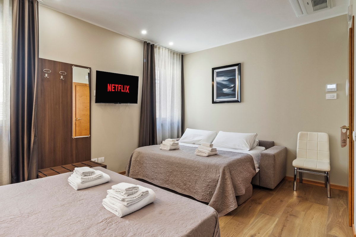 A hotel room with two beds, a TV, a framed picture, and a bedside table with towels.