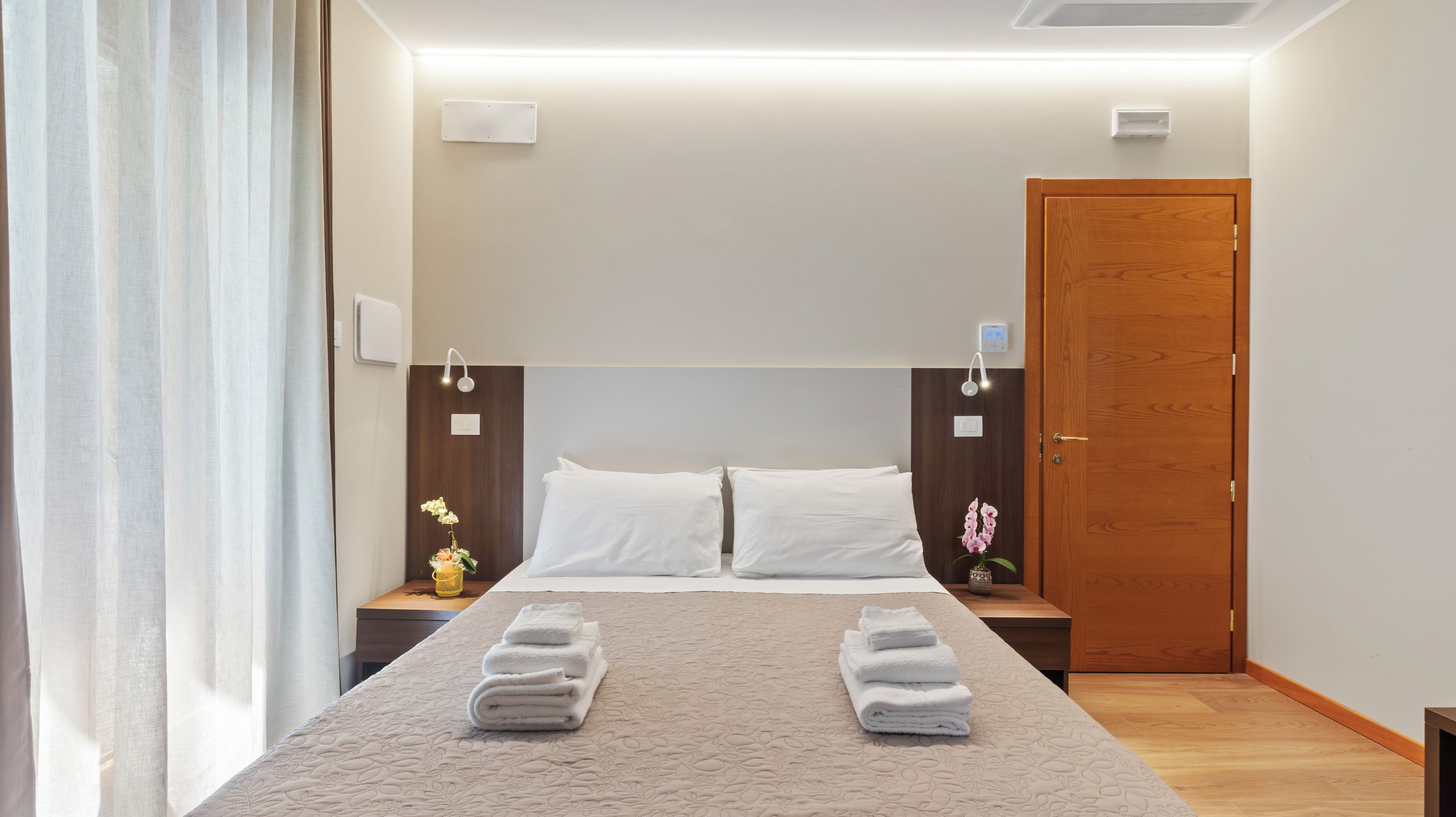 Ein Hotelzimmer mit einem Bett, zwei Nachttischen, einer Holztür und einem Beistelltisch mit einem Blumenstrauß.
