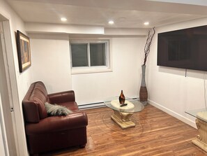 A living room with a brown leather sofa, a glass coffee table, a vase, and a flat-screen TV mounted on the wall. - 2 Bedroom Apartment Ahuntsic (Montreal)
