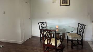 A dining area with a glass table surrounded by wooden chairs, a small orange candle, and a framed picture on the wall.