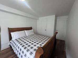 A bedroom with a wooden bed, white walls, and a checkered bedspread. - 2 Bedroom Apartment Ahuntsic (Montreal)