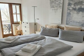 A hotel room with two beds, checkered bedding, a radiator, a desk, and a window with a view of the outside. - Small holiday home Allgäublick (Bad HIndelang)