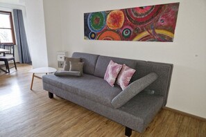 A living room with a grey sofa, a small round table, and a colorful abstract painting on the wall. - Small holiday home Allgäublick (Bad HIndelang)