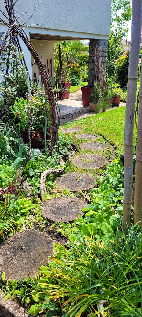 Ein Gartenpfad führt zu einem Haus mit einer Steinmauer und Kübelpflanzen.