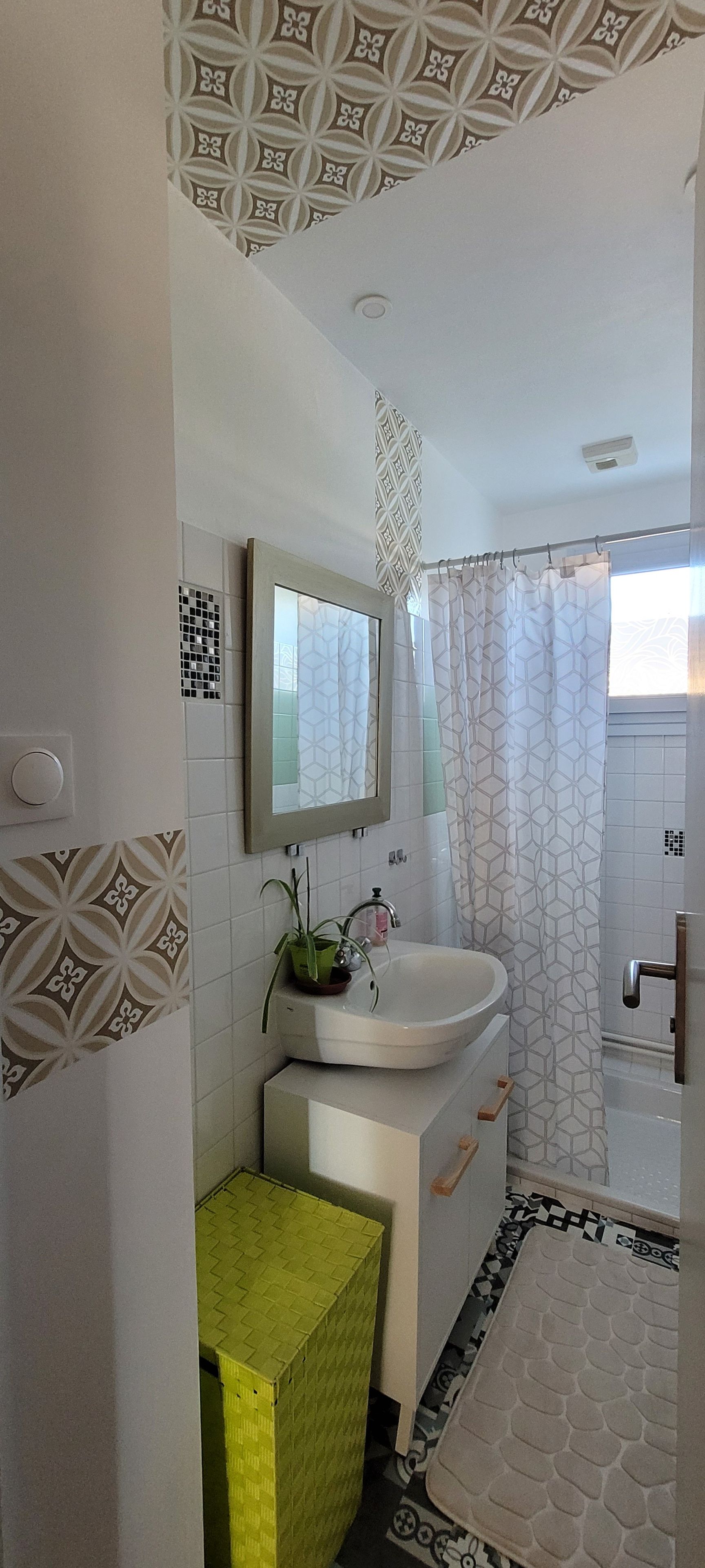 Une salle de bain avec un lavabo blanc, un miroir, un rideau de douche et des carreaux décoratifs sur les murs.