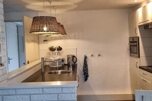A modern kitchen with a stainless steel sink, a hanging light fixture, and a built-in oven. - Holiday home in Ouddorp with swimming pool (Ouddorp)