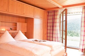 Ein Schlafzimmer mit zwei Betten, Holzschränken, einem Fenster mit Vorhängen und Blick auf eine bewaldete Landschaft.