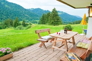 A wooden table and bench set on a brick patio with a view of a green valley and mountains. - Holiday apartment with 1 bedroom (Balderschwang)