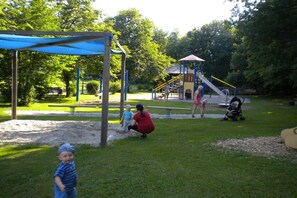 Une aire de jeux avec un toboggan, des balançoires et un espace abrité.