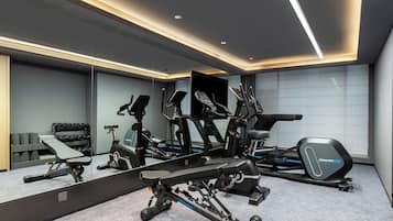 Un gimnasio moderno en casa con equipo de ejercicio, un espejo grande y un piso alfombrado gris.