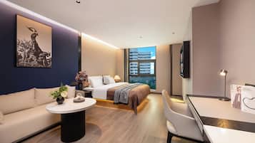 Habitación de hotel moderna con cama, sofá, escritorio y ventana grande con vista a la ciudad.
