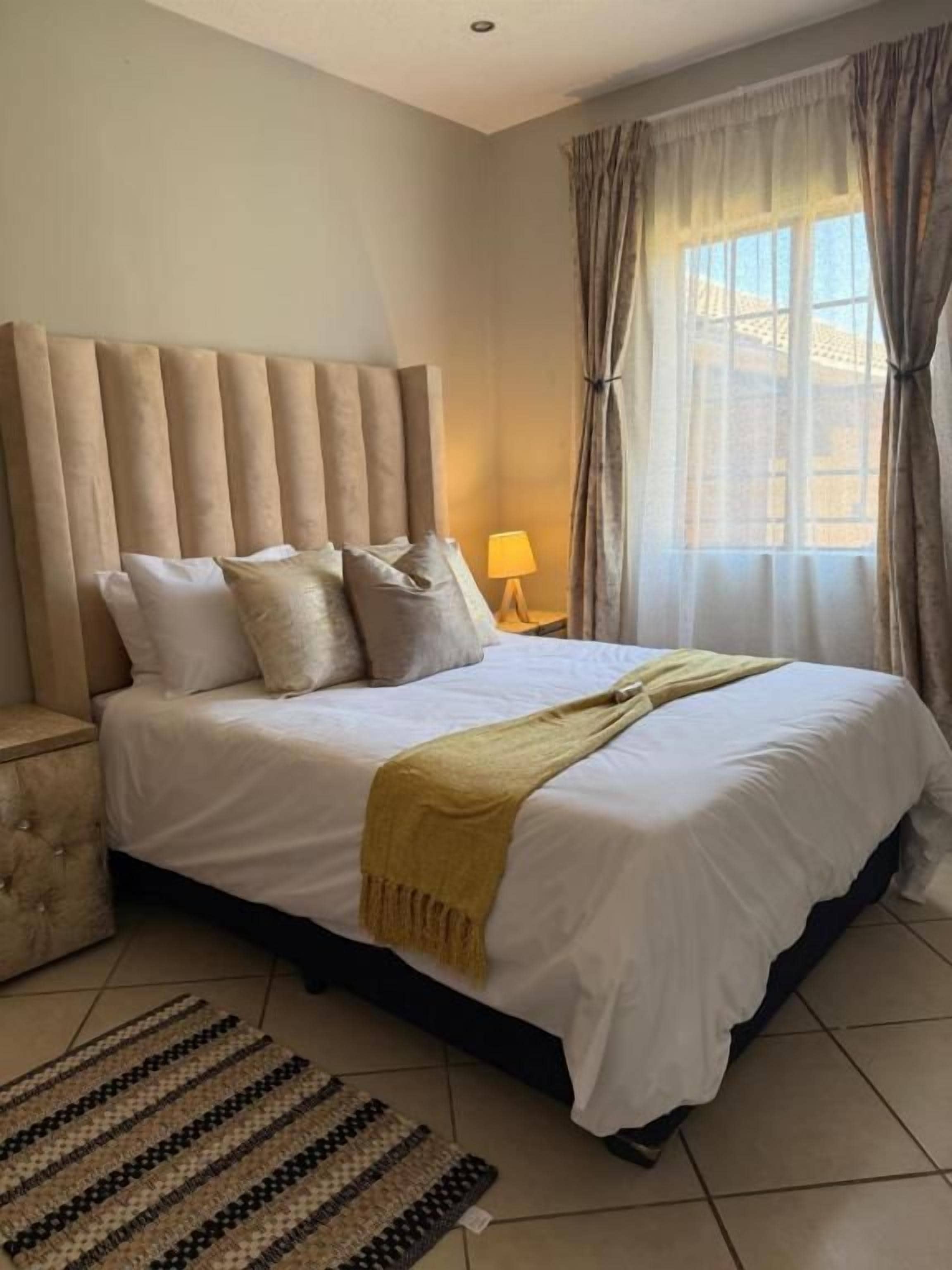 A hotel room with a large bed, a nightstand, a lamp, and a window with curtains.