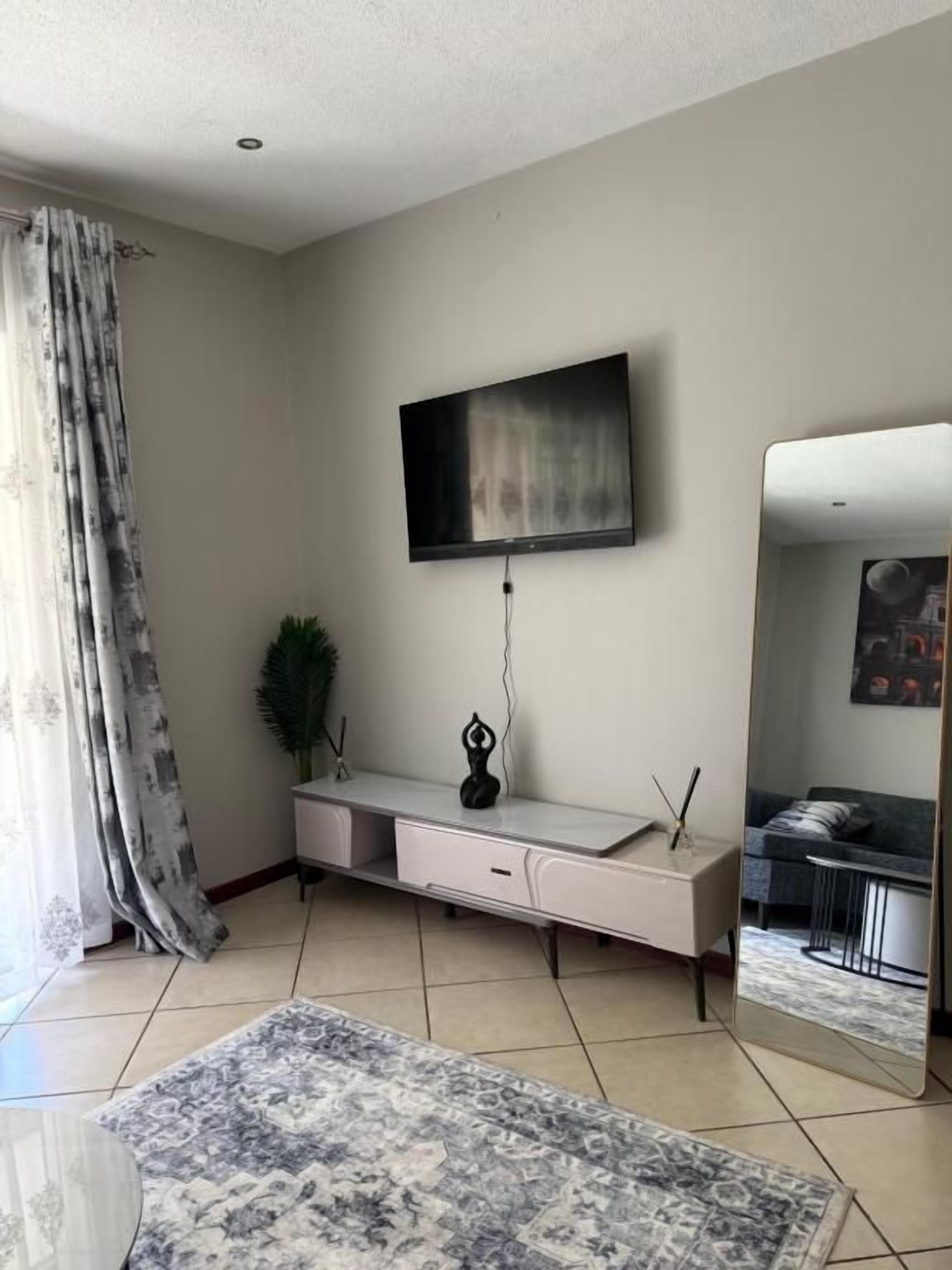 A modern living room with a flat-screen TV mounted on the wall, a console table with drawers, a large mirror, and a patterned rug on the floor.