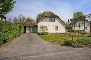 A single-story house with a paved driveway leading to the entrance, surrounded by a well-maintained lawn and a hedge.