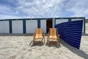 Twee strandstoelen voor een gebouw met een blauw luifel.