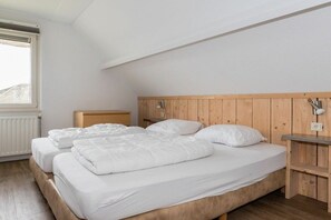 Een slaapkamer met een houten hoofdbord, twee bedden, een nachtkastje en een raam.