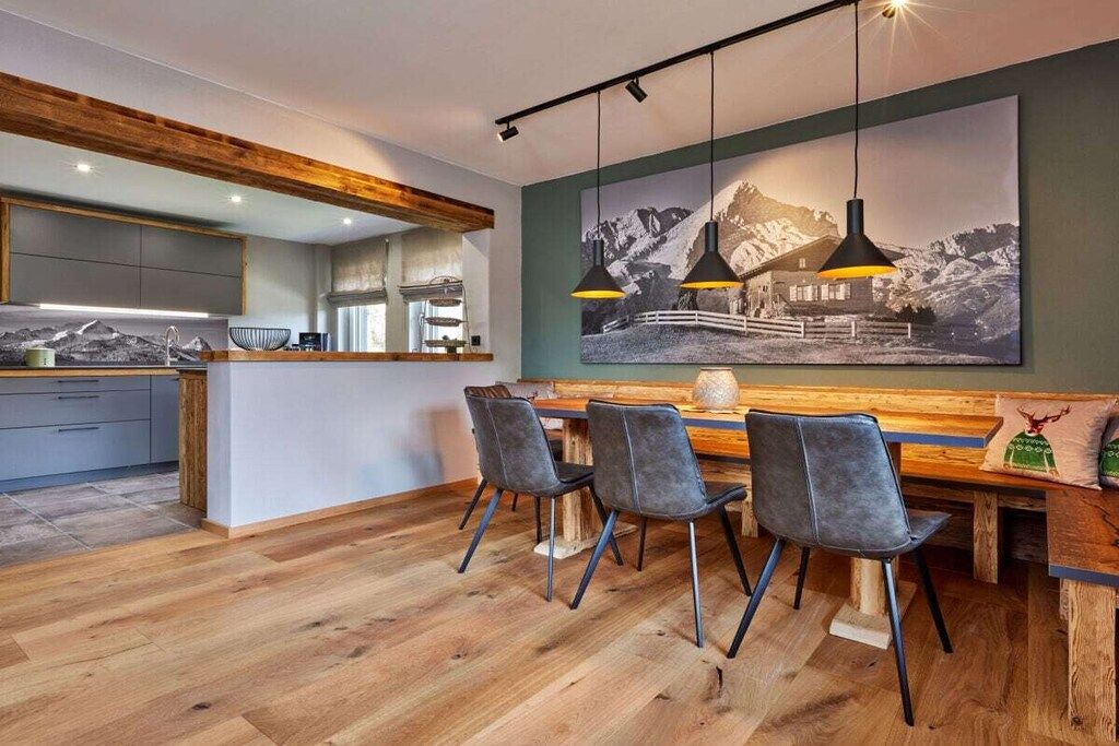 A modern kitchen with a wooden island, a dining area with chairs, and a large framed photograph on the wall.