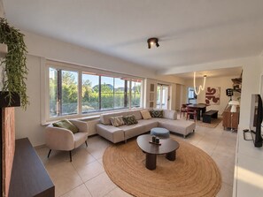 A modern living room with a sectional sofa, a round coffee table, and a dining area with a table and chairs. - Bright, spacious home with a garden near Brussels (Zaventem)