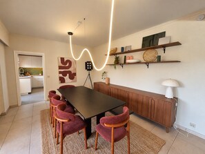 A dining area with a long table, six chairs, a wooden cabinet, and a wall-mounted shelf with decorative items. - Bright, spacious home with a garden near Brussels (Zaventem)