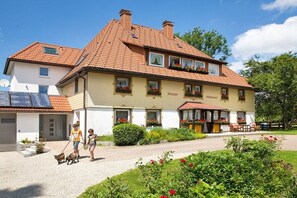 Ein zweistöckiges Gebäude mit rotem Ziegeldach, einem Garten mit roten Blumen und einem gepflasterten Auffahrt.