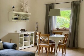 A dining area with a white table, wooden chairs, a white cabinet, and a window with curtains. - Holiday home in Pluwig with swimming pool (Pluwig)