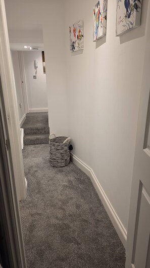 A hallway with carpeted stairs, a woven basket, and two wall-mounted artworks. - Stylish Stay in Brighton London Road Gem (Brighton and Hove)