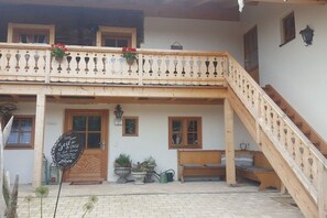 Una cabaña tradicional con una escalera de madera, un balcón con macetas de flores y un banco en el exterior.