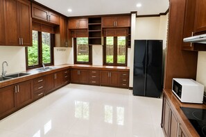 A modern kitchen with wooden cabinets, a black refrigerator, a white microwave, and a stainless steel sink. - Private 5-Bedroom Pool Villa in Middle of the Island Phuket (Tambon Kathu)