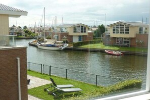 A canal view with a boat docked, a small inflatable boat, and residential buildings with large windows. - Water Villa Lisdodde (Workum)