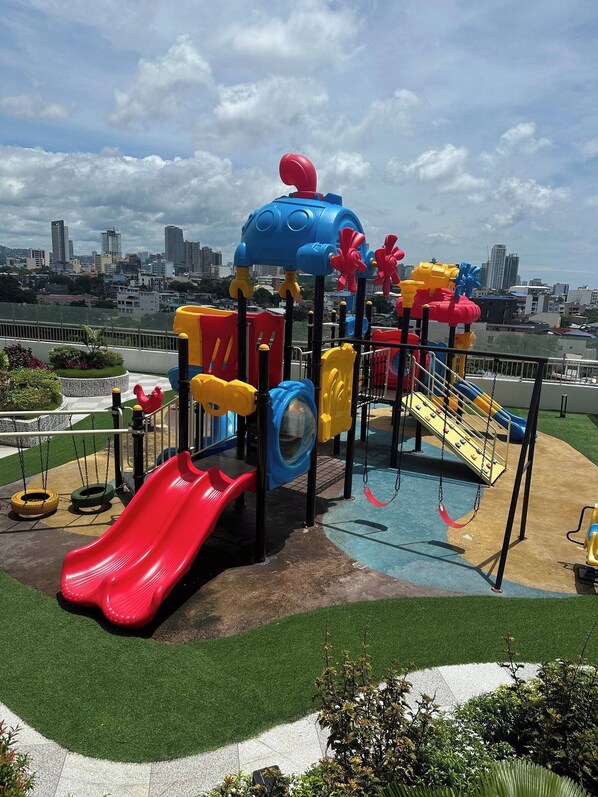 A playground with slides and swings, surrounded by green grass and a cityscape in the background. - Fully furnished, modern Condo unit in ARC tower-Cebu City (Cebu City)