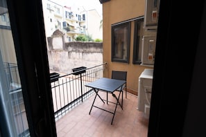 A balcony with a table and chairs, a window, and a wall-mounted air conditioning unit. - Charming Catania Apartment with Balcony (Città metropolitana di Catania)