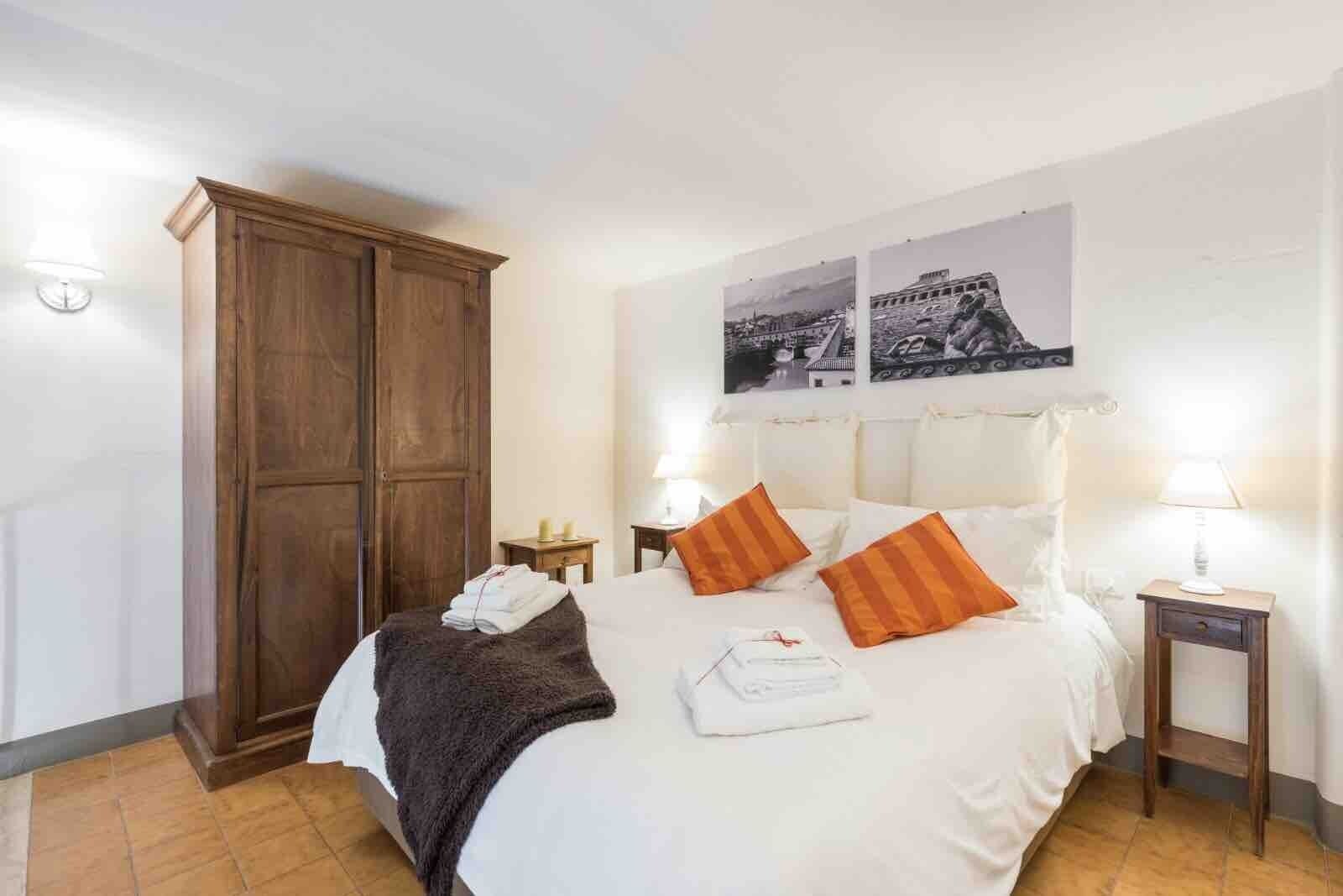 A hotel room with a bed, two nightstands, a wooden wardrobe, and two wall-mounted pictures.