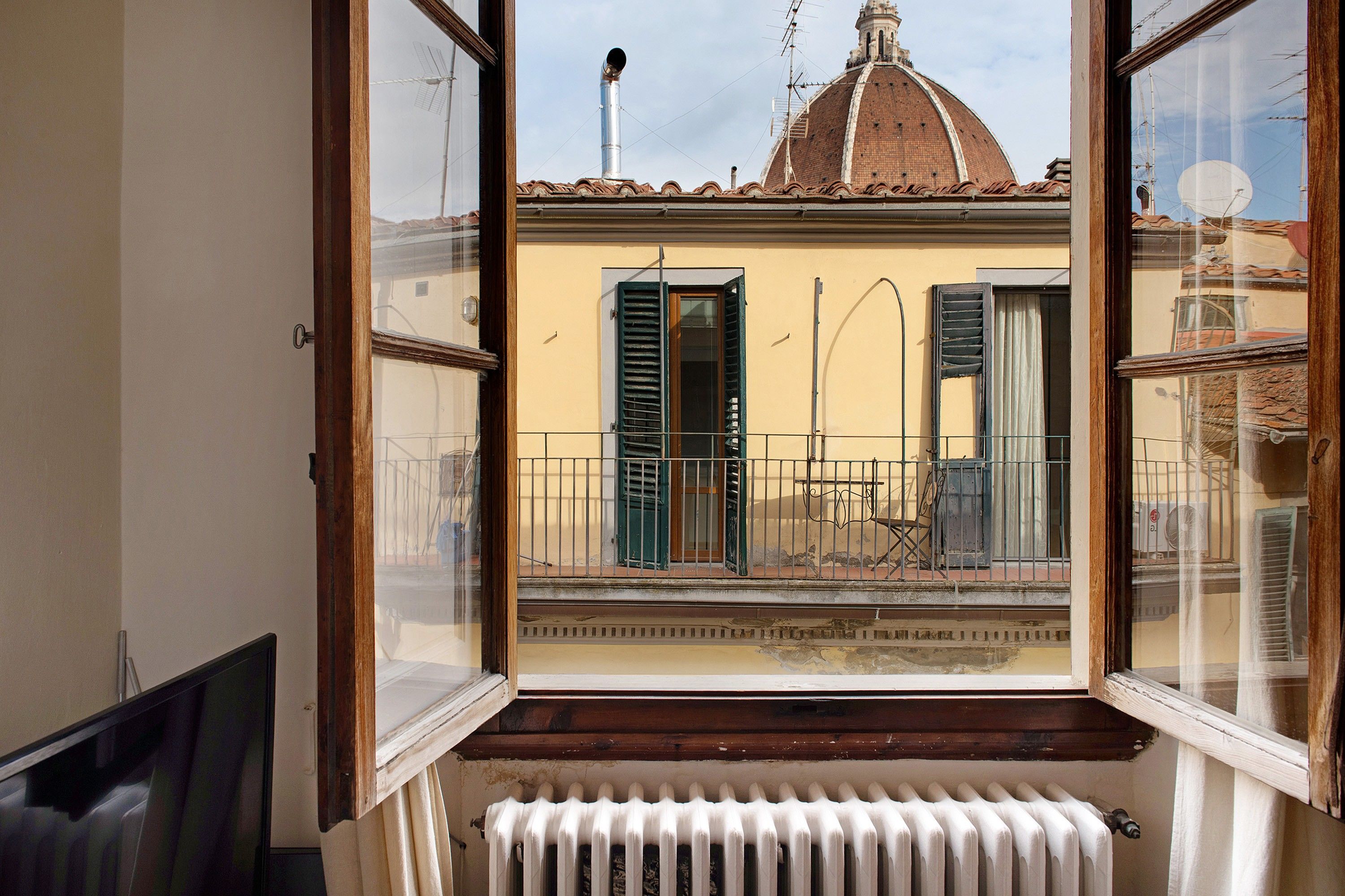 Ein Zimmer mit Blick auf ein Gebäude mit einer Kuppel und Antennen, einem Heizkörper und einem Fenster mit Rollläden.