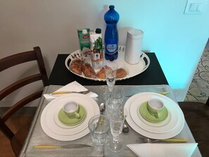 Ein Esstisch mit Tellern, Tassen, Besteck, einem Glas und einer Platte mit Brot und Getränken.