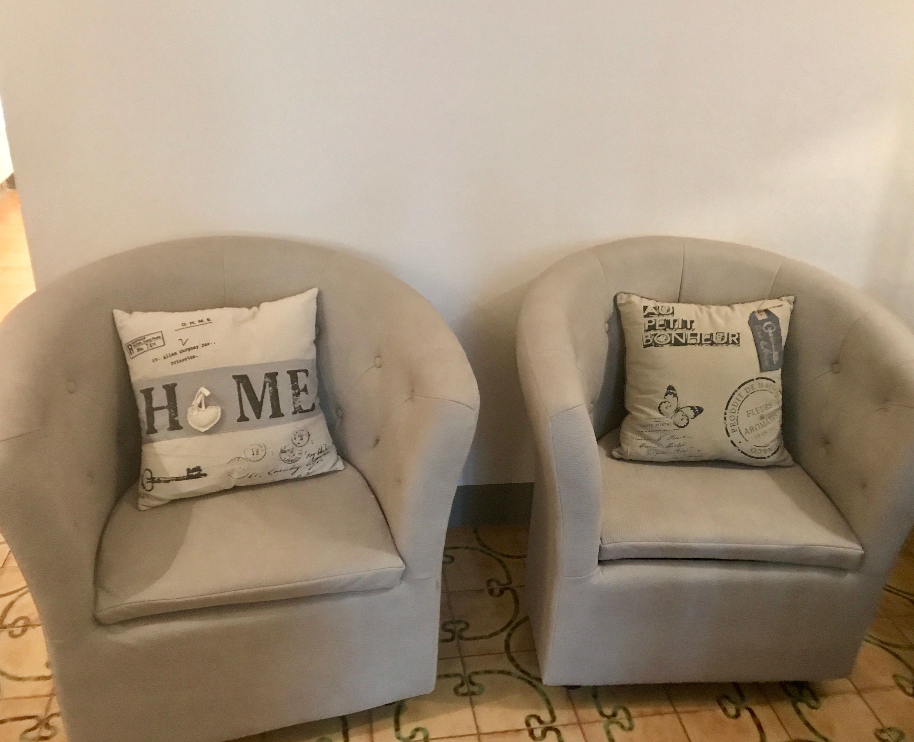 Two armchairs with decorative pillows against a plain wall.