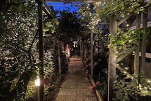 A garden pathway with a wooden pergola structure, surrounded by various plants and flowers. - Apartments Zandvoort (Zandvoort)