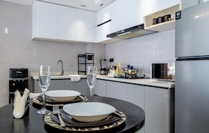 A modern kitchen with a dining area set for two, featuring a water dispenser, a coffee machine, and a built-in oven. - 1-Bedroom Apartment with Nairobi National Park Views (Nairobi)