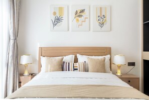 Una cama bien hecha con cabecera de madera, flanqueada por dos mesitas de noche con lámparas, y tres obras de arte colgadas en la pared.