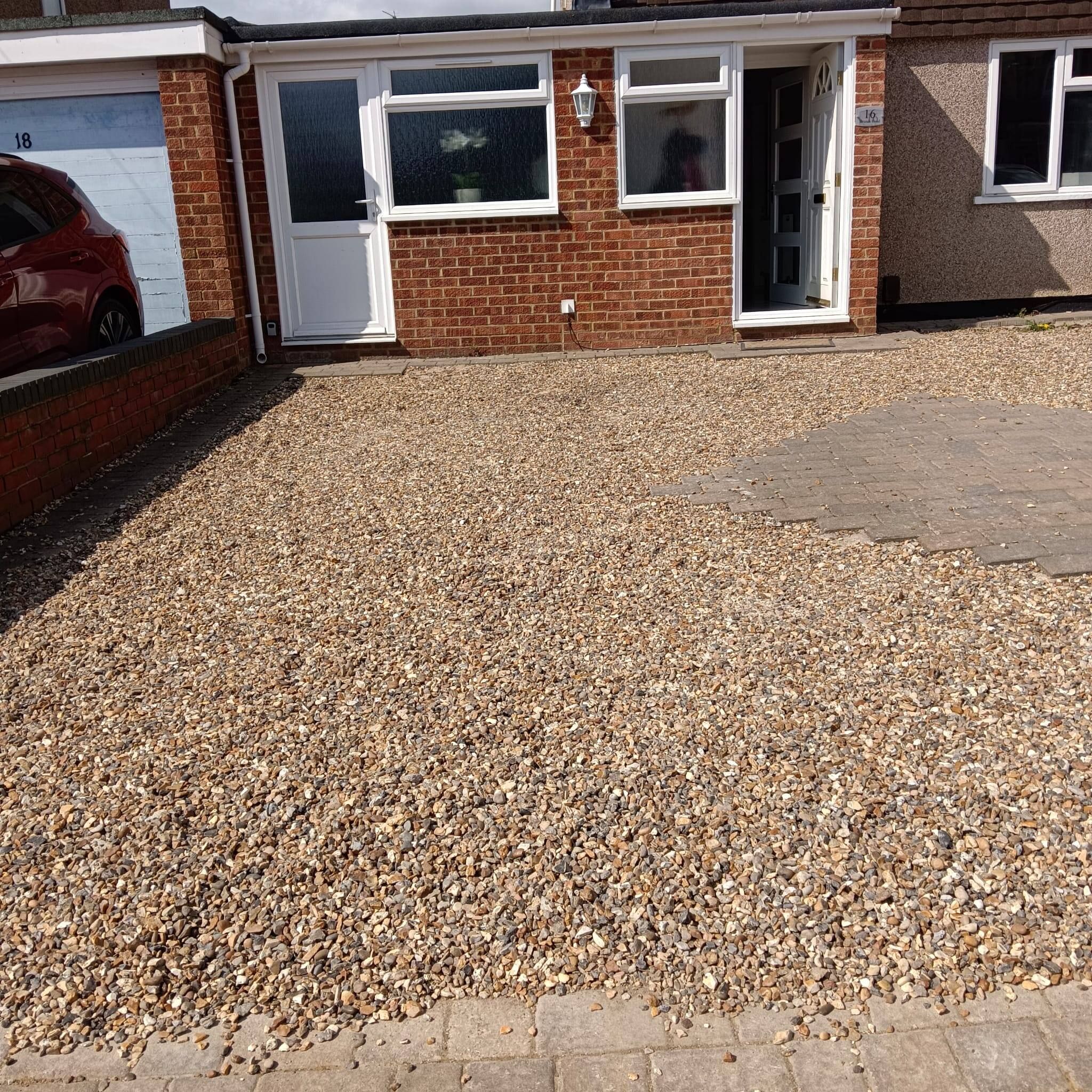 A residential building with a gravel driveway, a garage, and a brick facade.